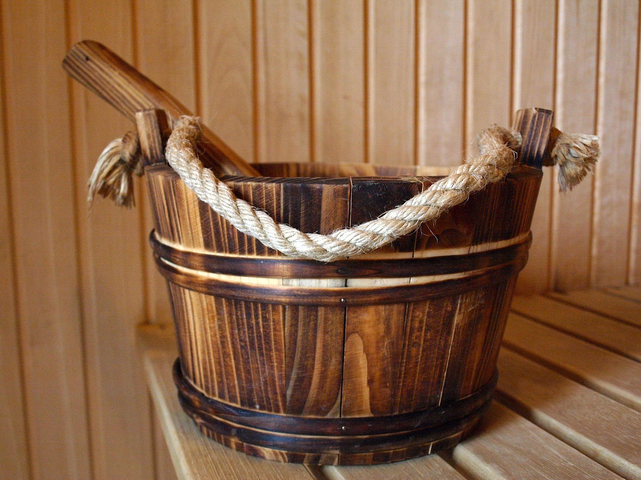 Saunakübel mit Holzkelle auf der Bank einer Holzsauna