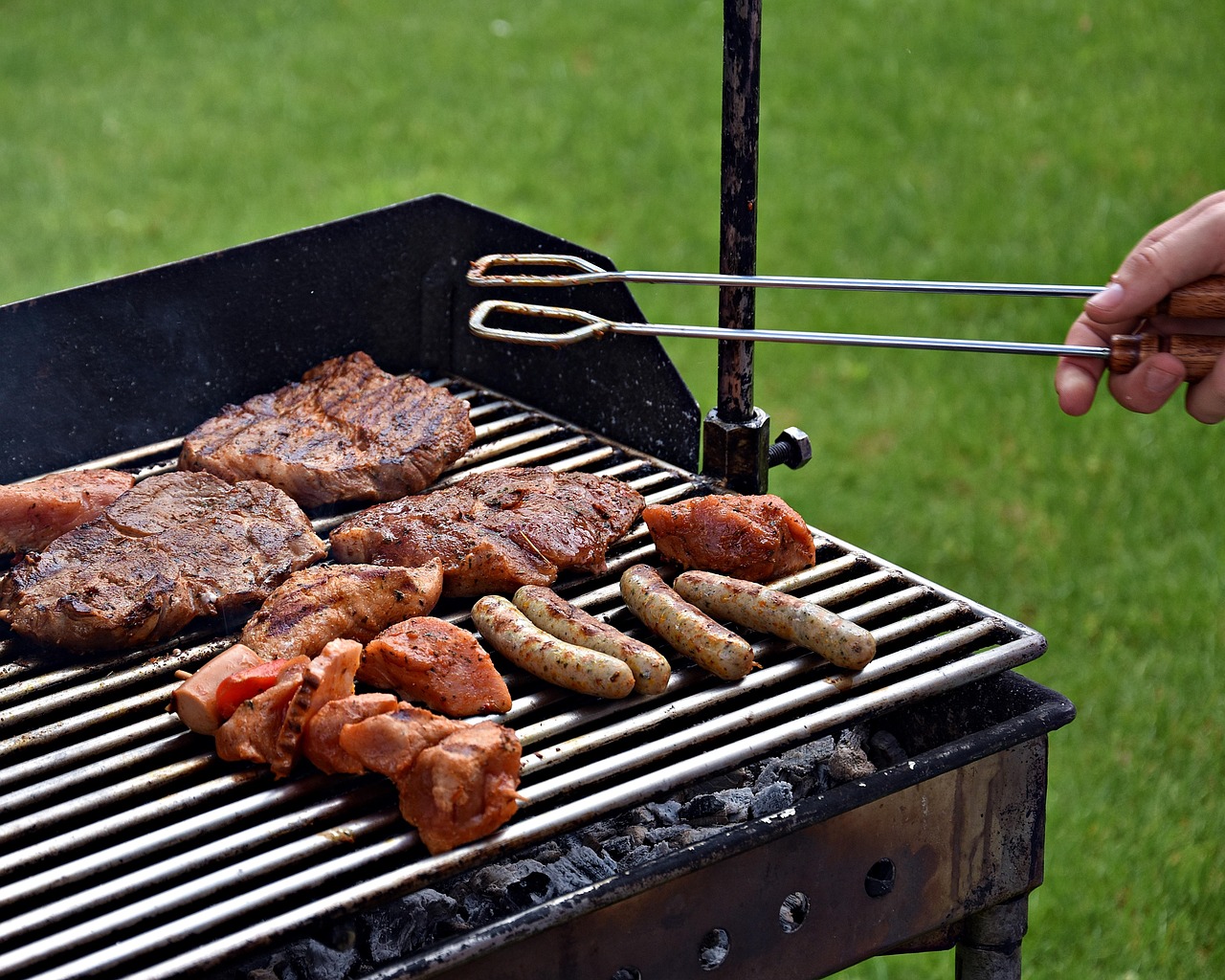 Holzkohlegrill mit Steaks und Würstchen, gewendet mit der Grillzange