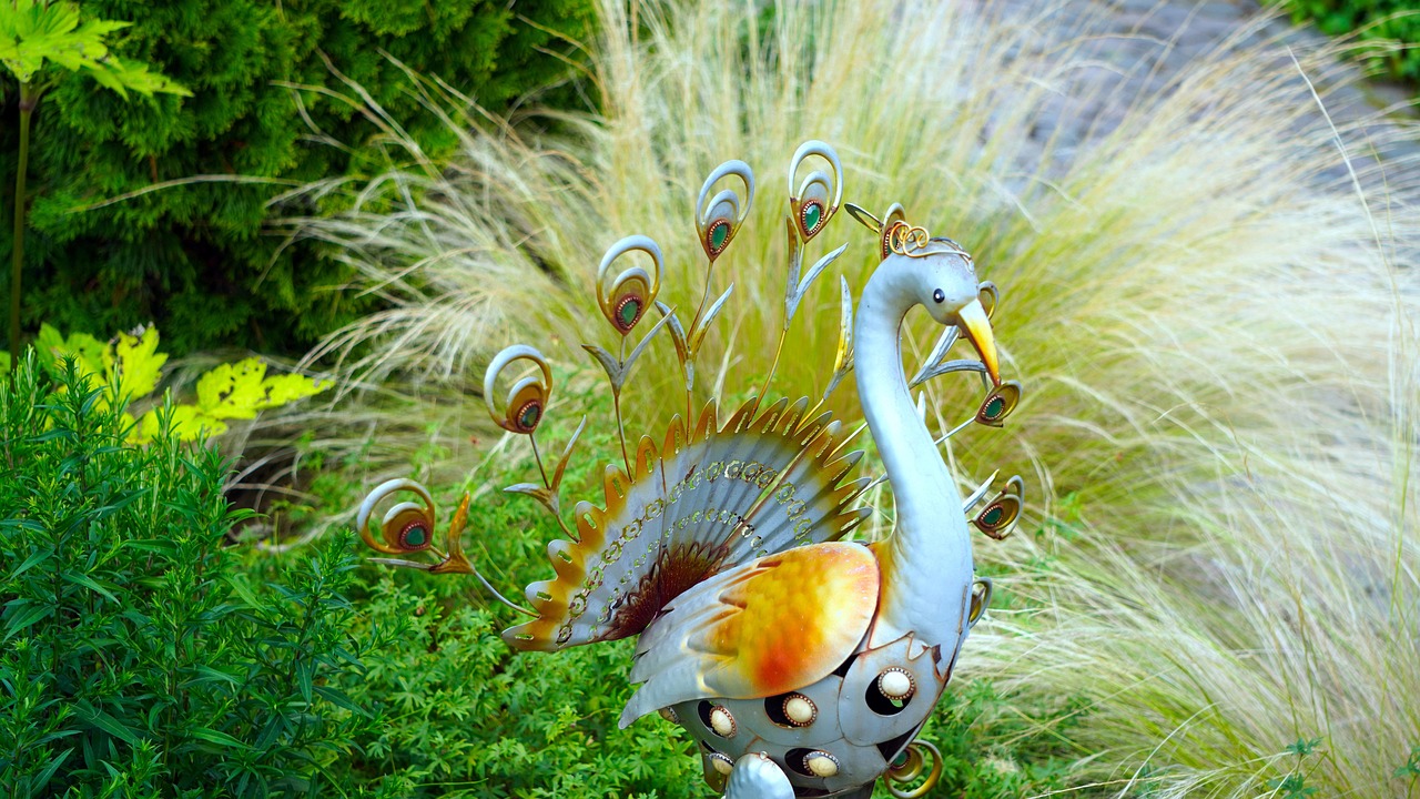 Bunter Metall-Pfau als Gartendeko zwischen Ziergräsern