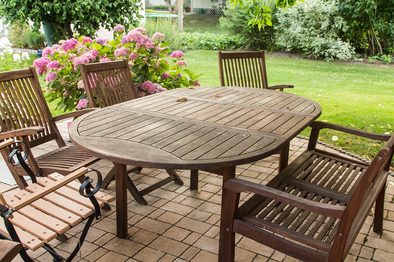 Holztisch mit Gartenstühlen auf einer Terrasse vor blühenden Hortensien