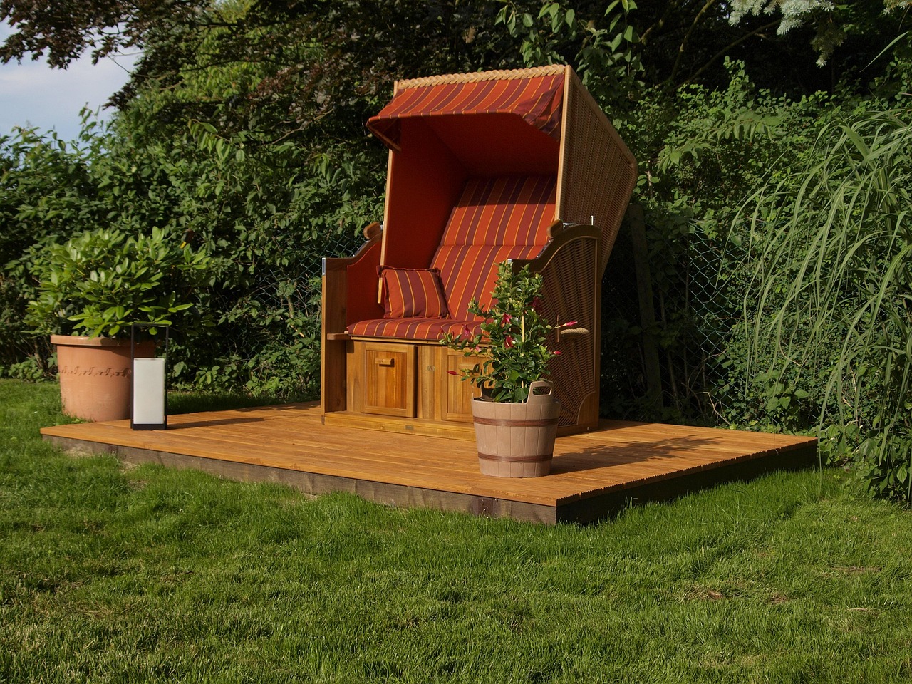 Strandkorb auf einem Holzpodest im Garten, umgeben von Kübelpflanzen und Rasen